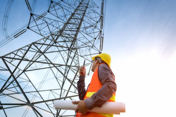 Construction worker checking location site near to High voltage tower. Construction worker checking location site near to High voltage tower.